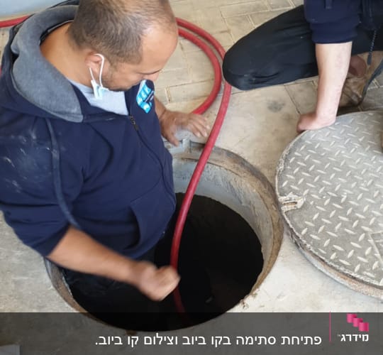 שני אנשים עובדים עם צינור אדום בבור ביוב